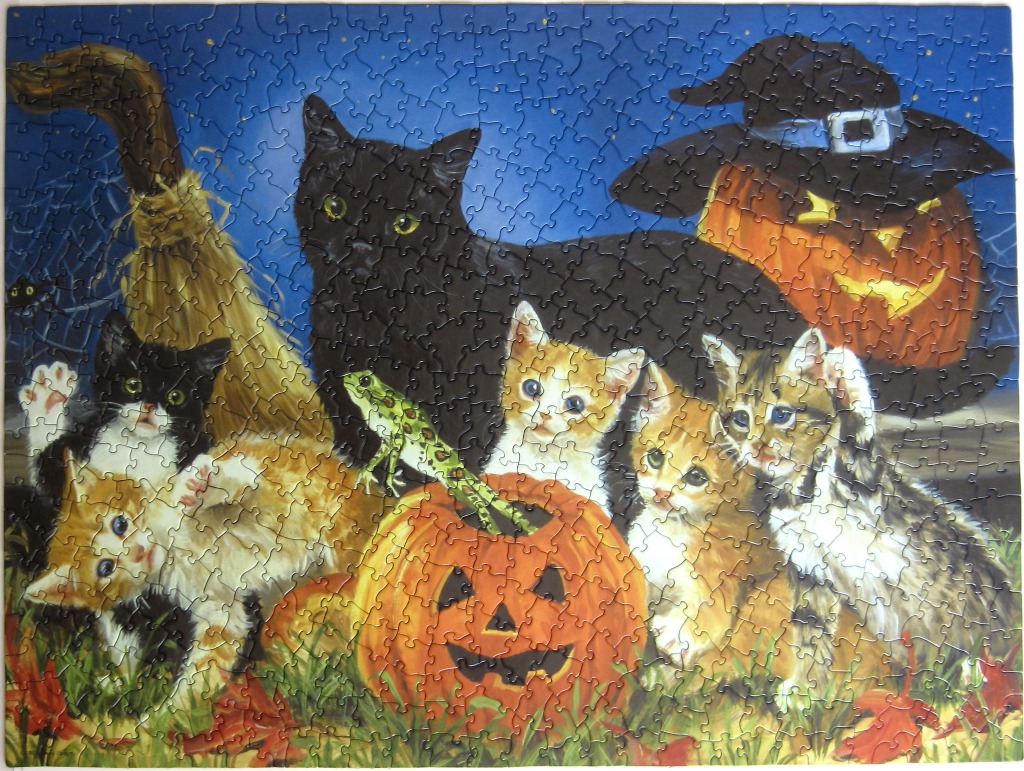 A group of kittens playing around a jack-o'-lantern, a broom, and a black cat against a night sky background.