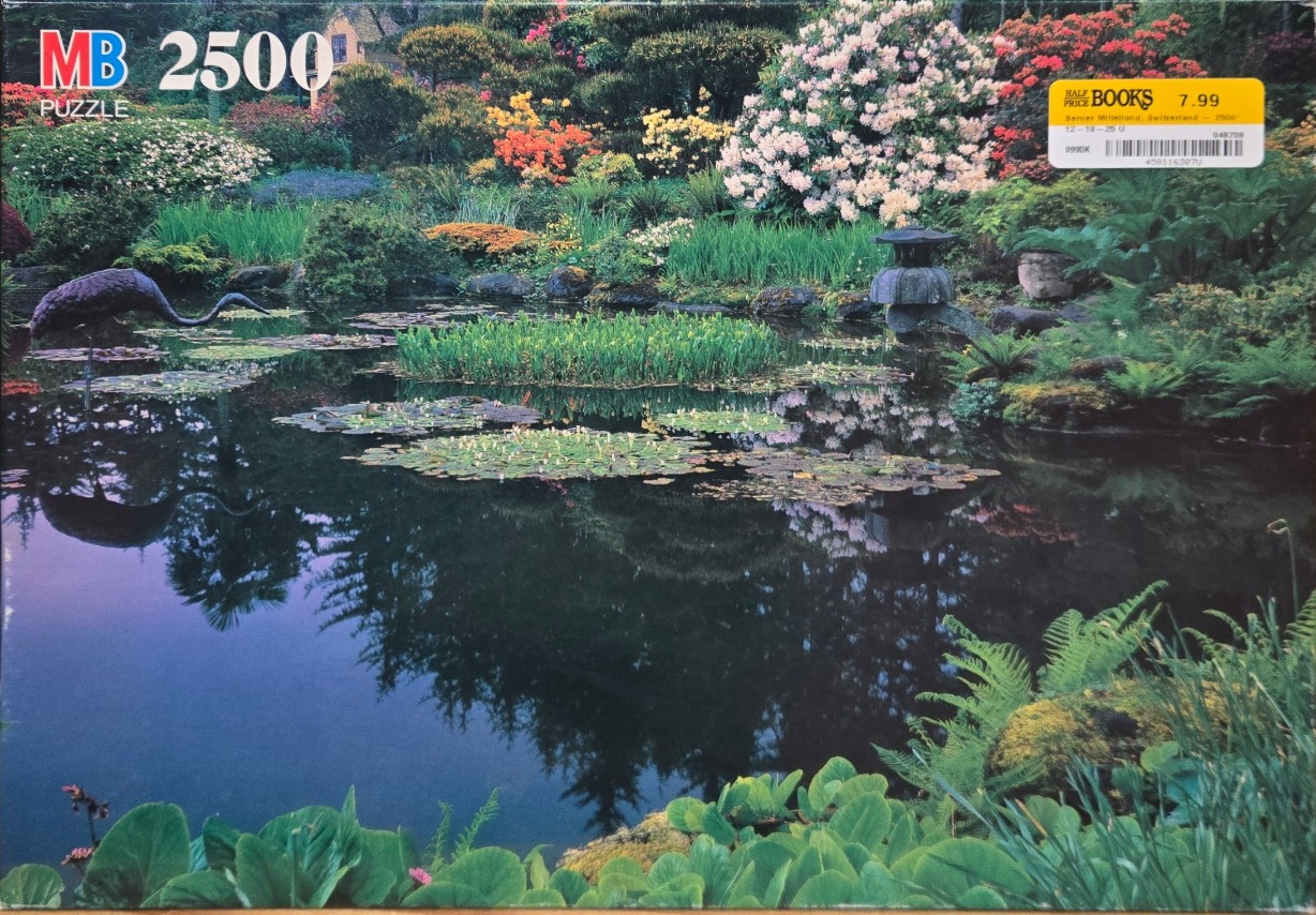 A serene pond in a lush garden filled with blooming rhododendrons, a crane sculpture, and a stone lantern.