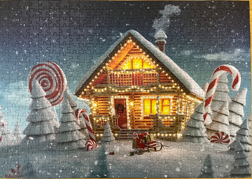 A cozy log cabin decorated with glowing Christmas lights in a snowy landscape with giant candy decorations.