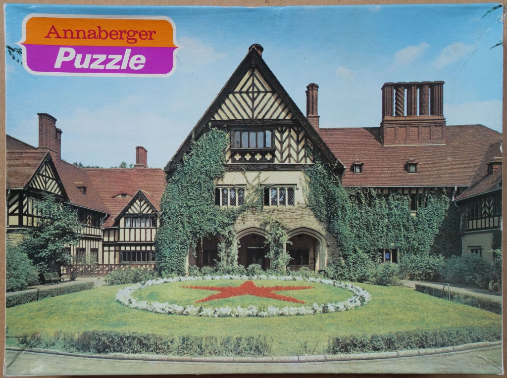 A sprawling Tudor-style manor house with ivy-covered stone walls and a red star flowerbed in the foreground.