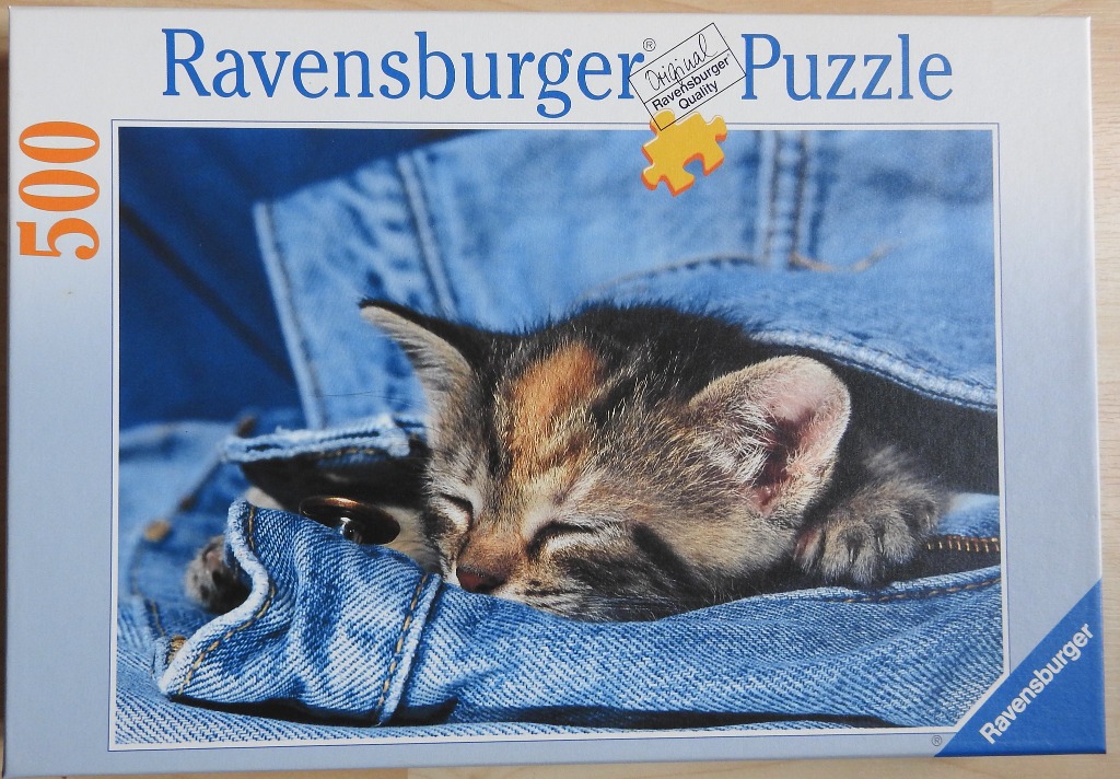 A close-up photograph of a tiny, sleepy calico kitten curled up and sleeping inside the pocket of a denim jacket.