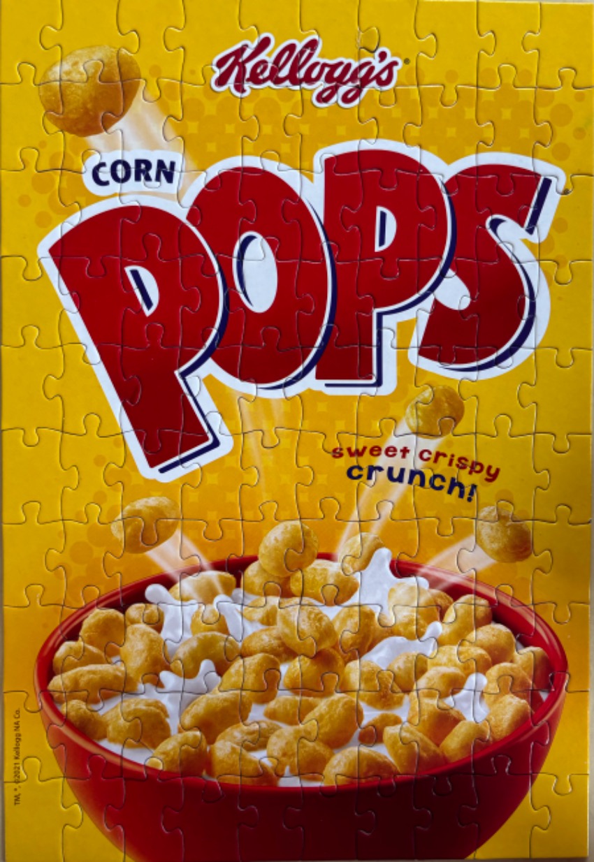 A close-up view of a Corn Pops cereal box illustration featuring a red bowl of cereal on a yellow background.