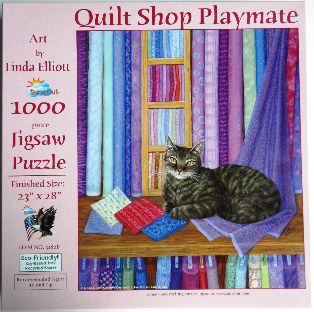 A tabby cat resting on a wooden shelf in front of colorful fabric bolts in a quilt shop.