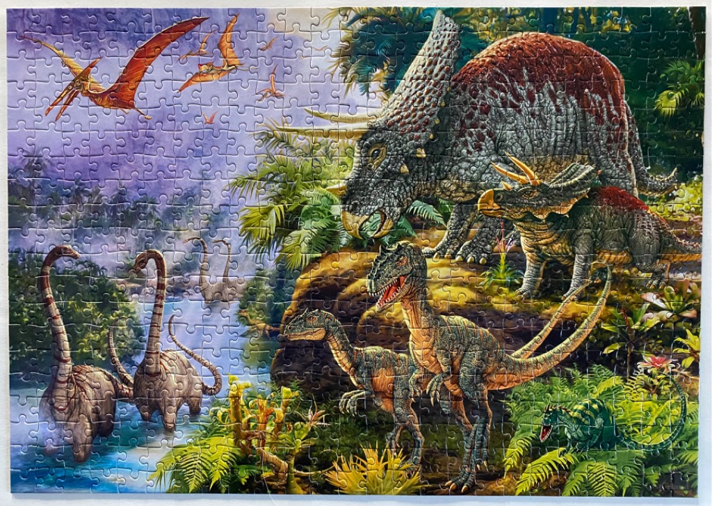 Prehistoric landscape featuring various dinosaurs including triceratops, raptors, and long-necked sauropods.