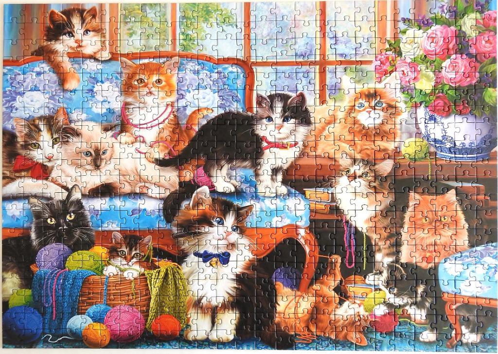 A group of adorable kittens playing around a blue sofa with a basket of yarn and a vase of flowers.