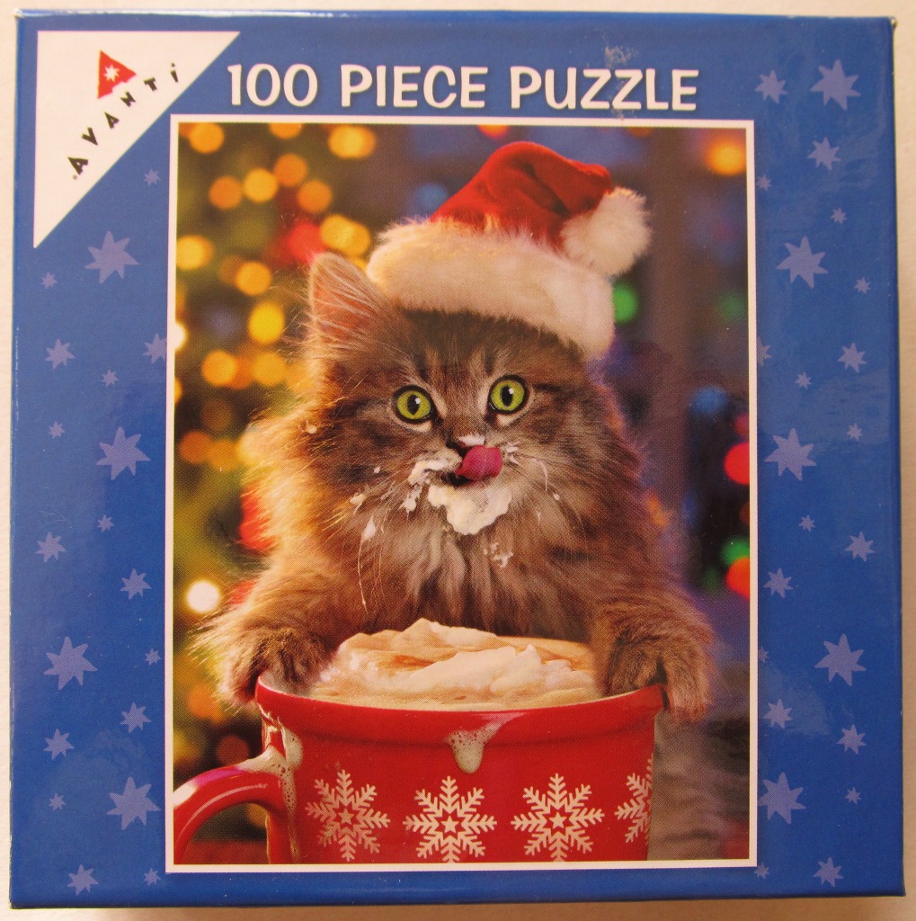A fluffy kitten wearing a Santa hat and licking whipped cream off its face, with a red mug in the foreground.