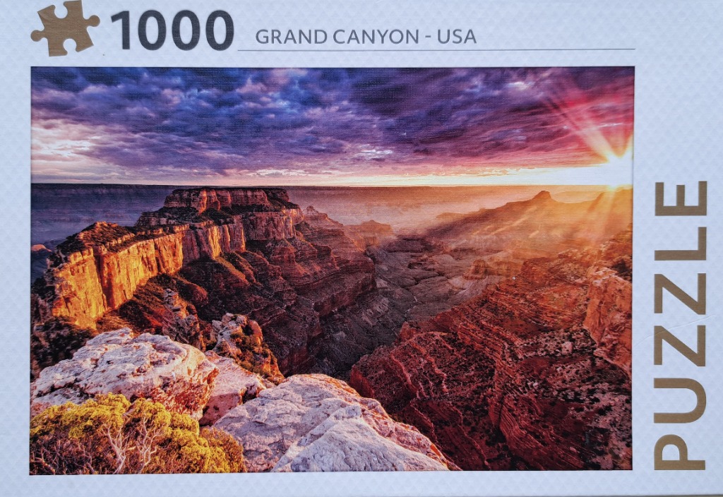 A panoramic landscape of the Grand Canyon at sunrise with purple, orange, and gold colors.
