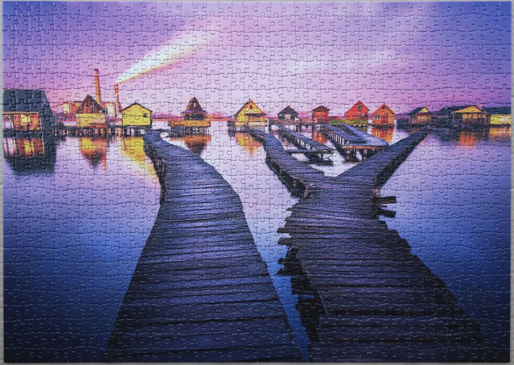 A row of colorful houses built on stilts over water with wooden walkways stretching toward them at twilight.