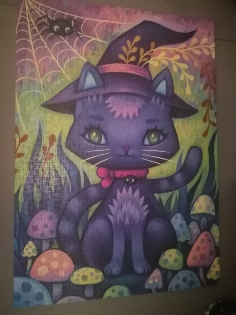 A whimsical illustration of a purple witch cat sitting among colorful mushrooms, with a spider and web in the background.