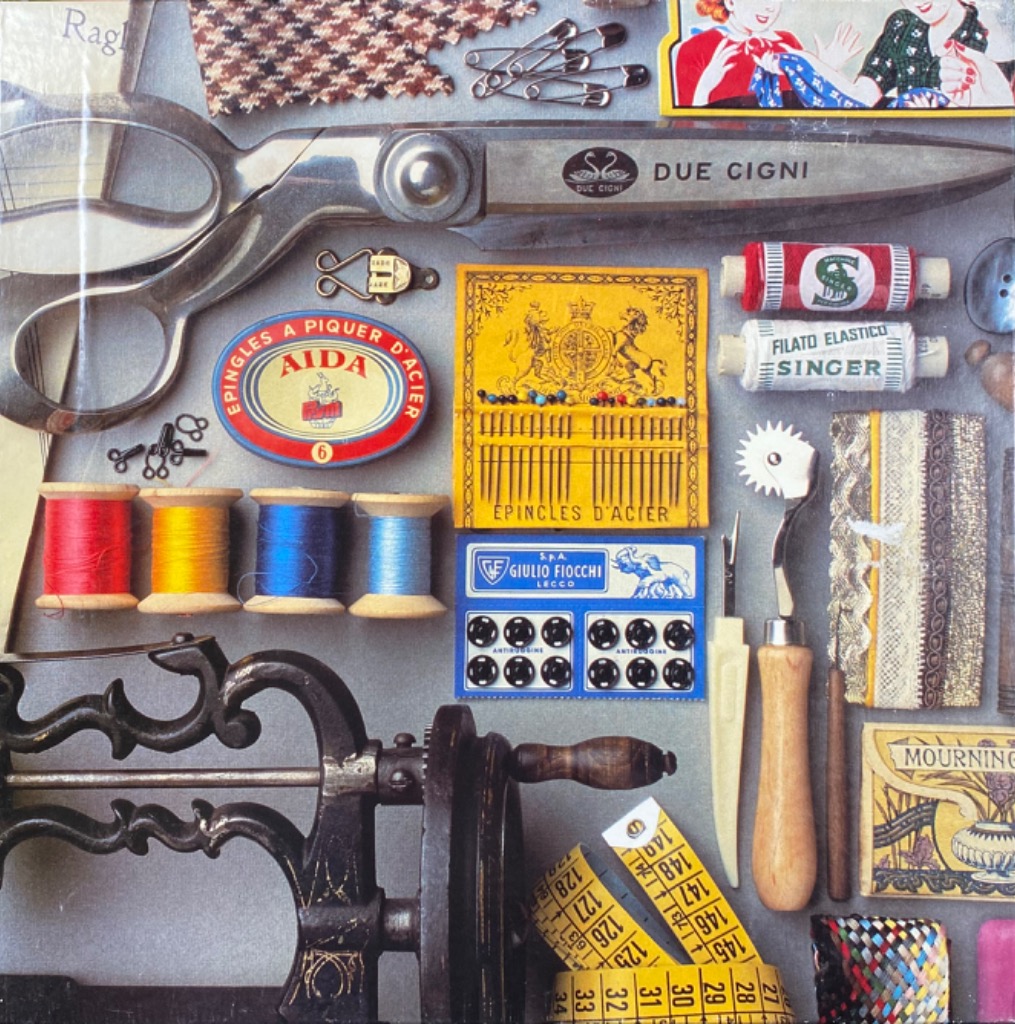 A flat-lay photograph of various vintage sewing tools and accessories arranged on a grey surface.