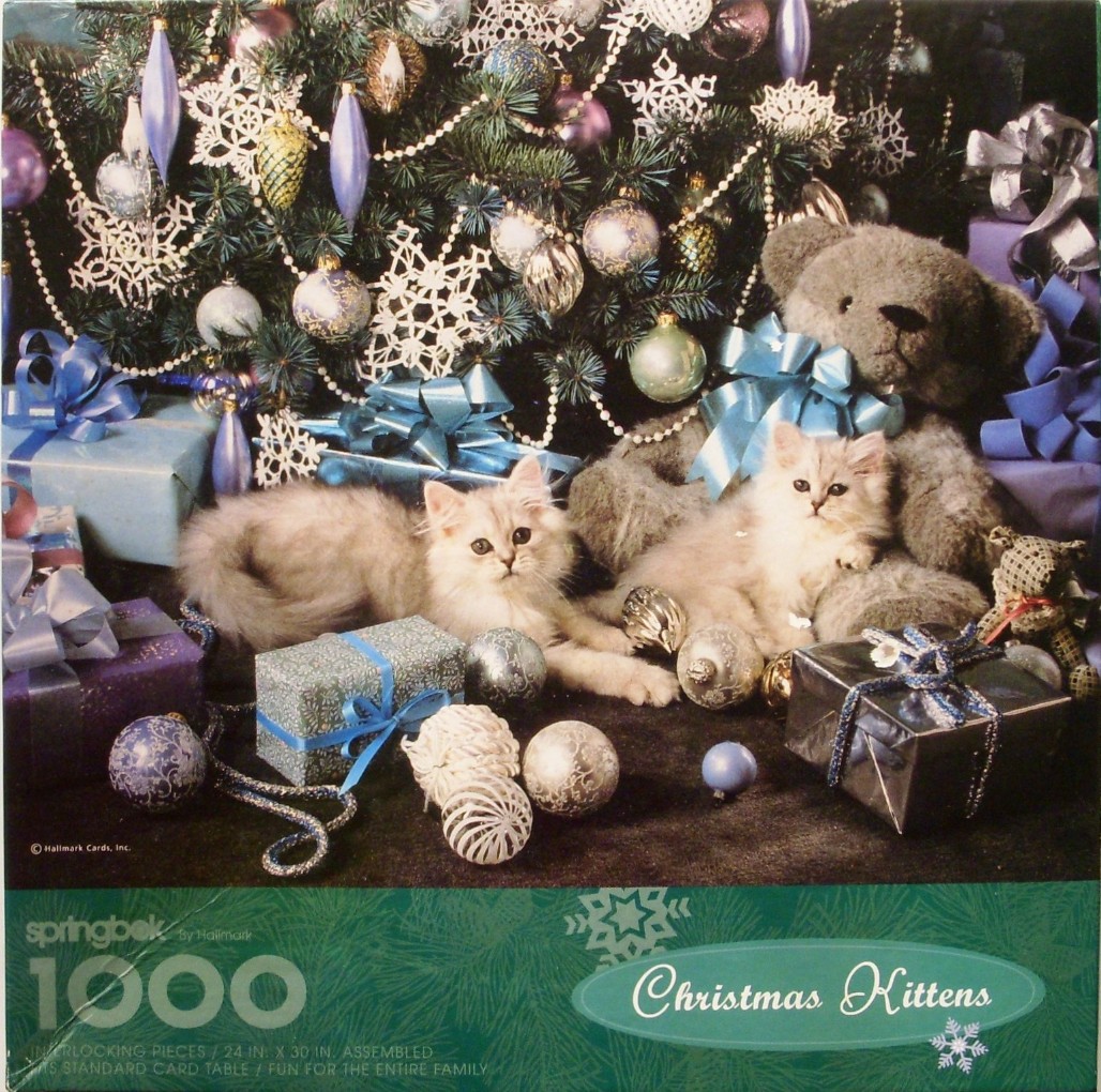 Two fluffy white kittens resting in front of a decorated Christmas tree with teddy bears and gift boxes.