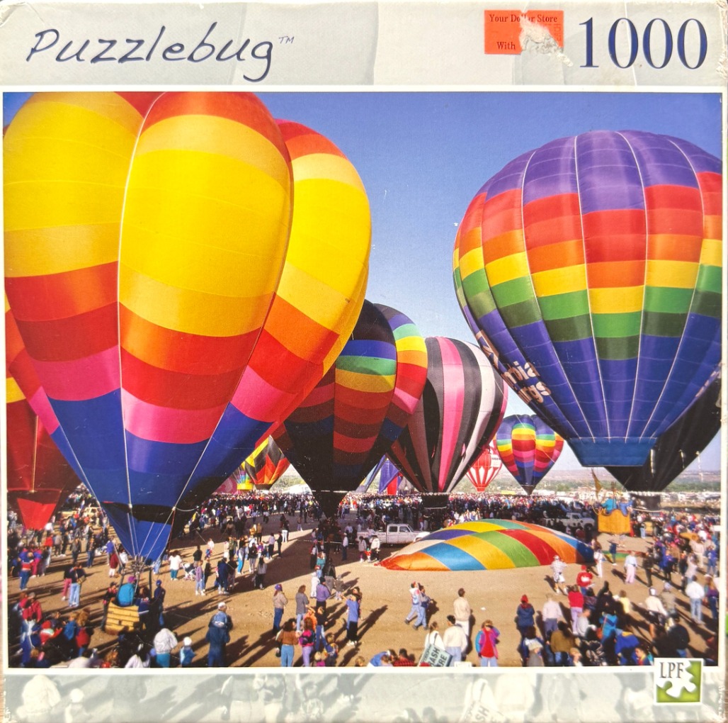 Several colorful hot air balloons tethered to the ground at a busy festival with crowds of people.