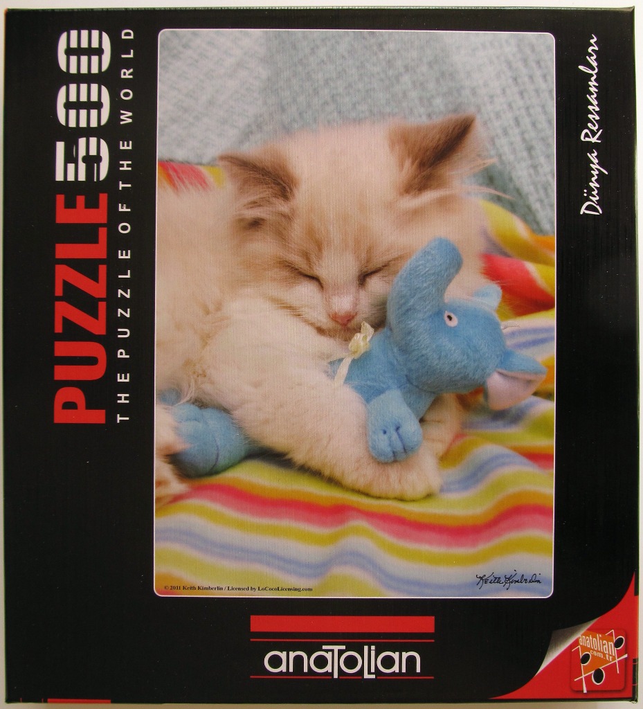 A fluffy cream-colored kitten sleeping while hugging a blue plush elephant toy on a striped blanket.