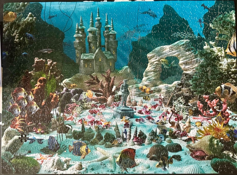 An underwater fantasy scene with a stone castle, a central statue, and various tropical fish.