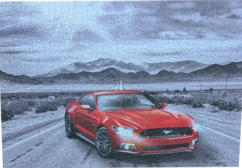 A bright red Ford Mustang parked on a desert highway against a black and white mountainous backdrop.