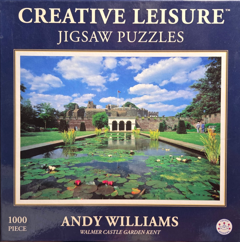 A photograph of a rectangular pond in front of a stone castle, surrounded by lush green lawns and lily pads.