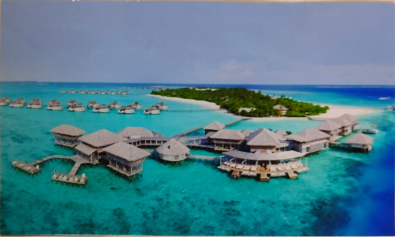 Aerial view of an overwater bungalow resort on a tropical island with turquoise lagoon.