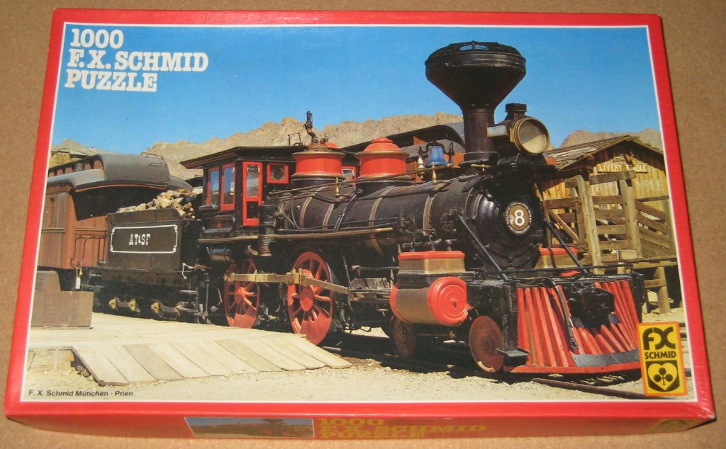 A vintage steam locomotive at a desert railway station under a bright blue sky.