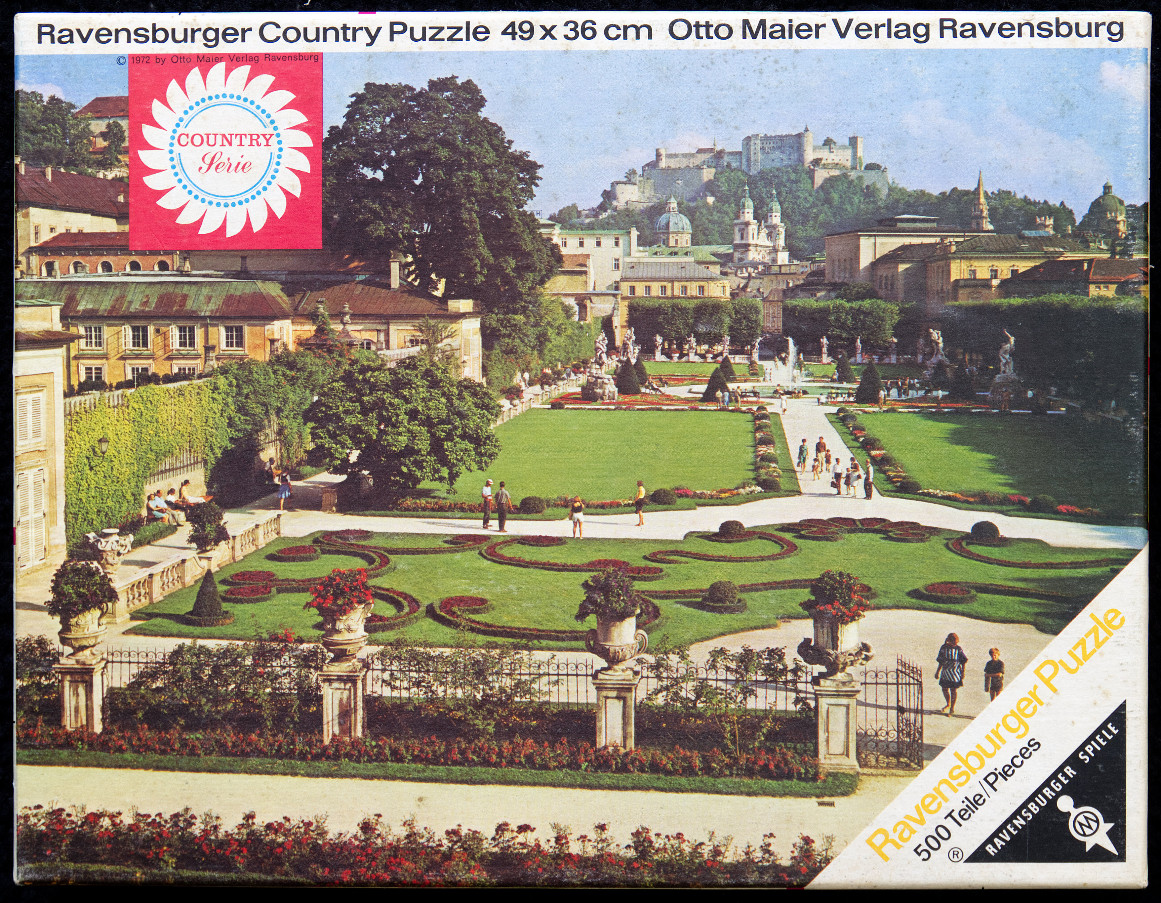 A sunny, vintage photograph of the Mirabell Gardens in Salzburg with a castle on the hill in the background.