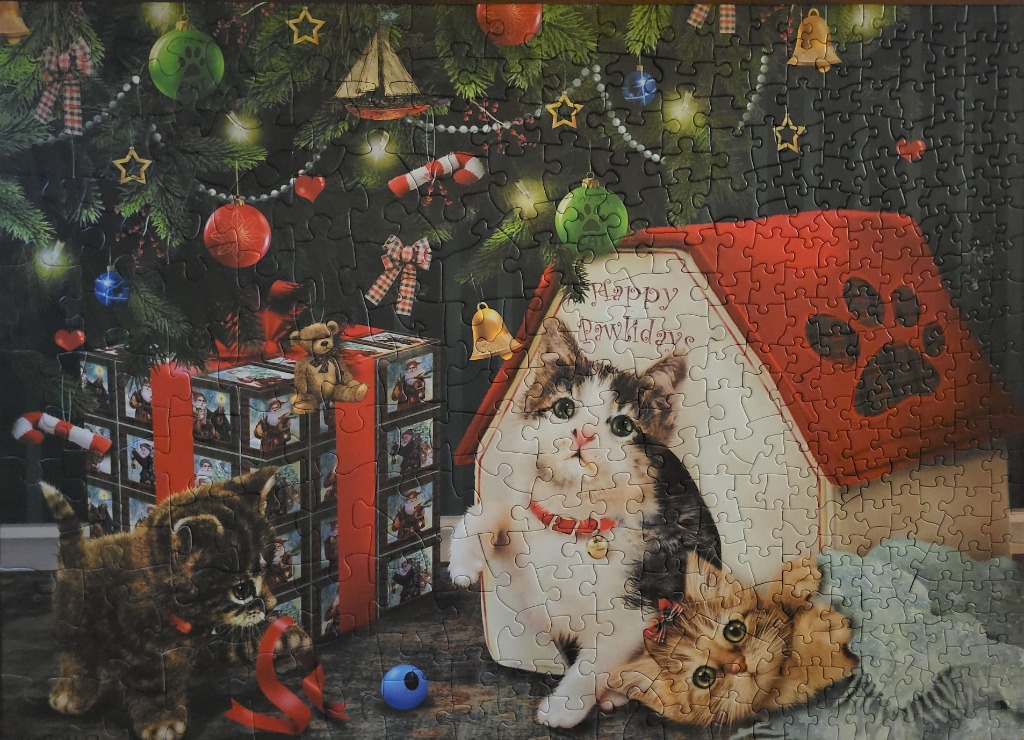 Three kittens celebrating Christmas with a decorated tree, gifts, and a pet house.