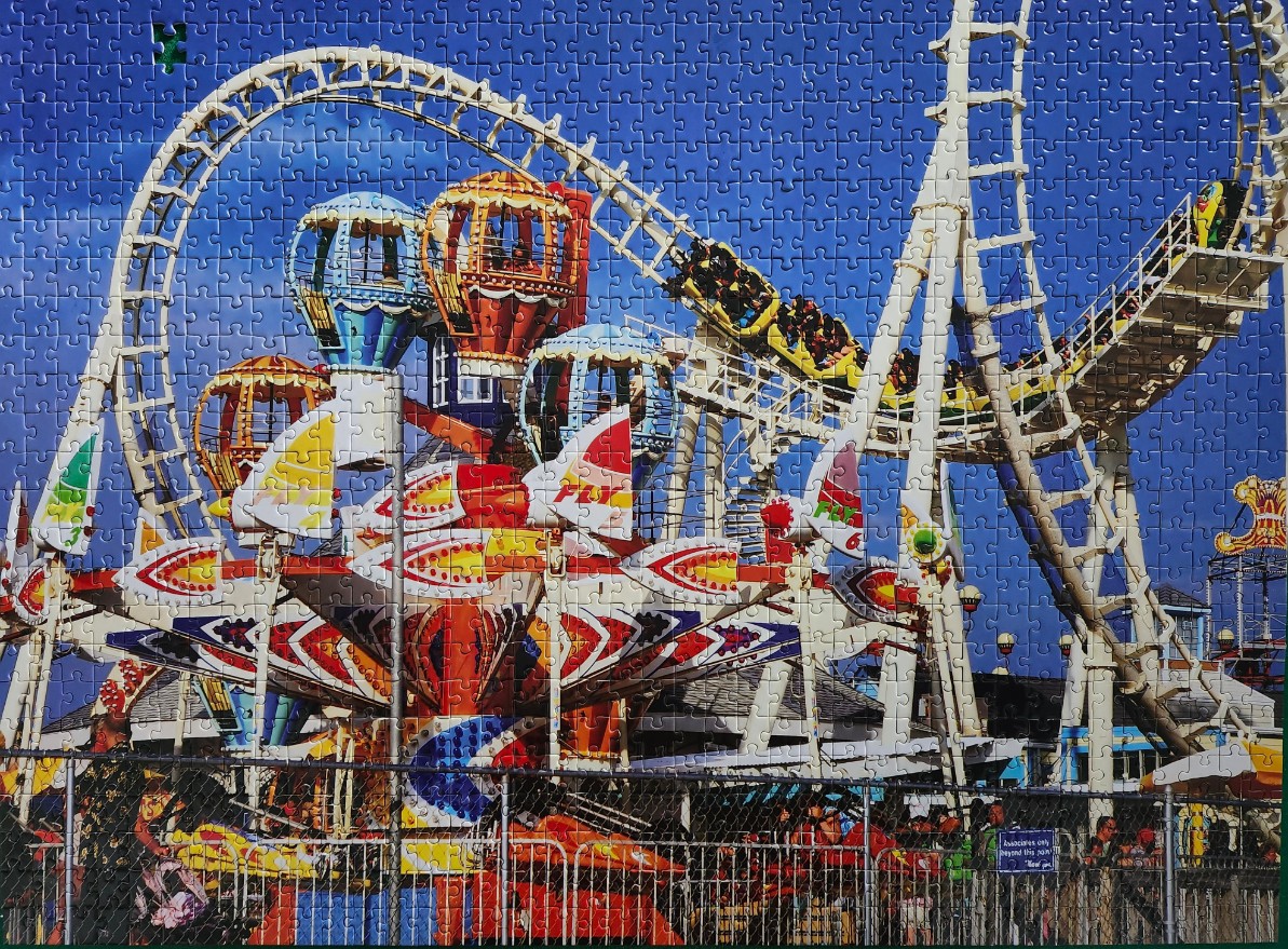 Amusement park scene featuring a bright yellow roller coaster and a multi-coloured spinning carousel ride.