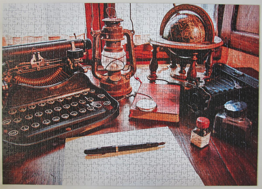 A vintage desk setup with an antique typewriter, globe, lantern, and writing implements.