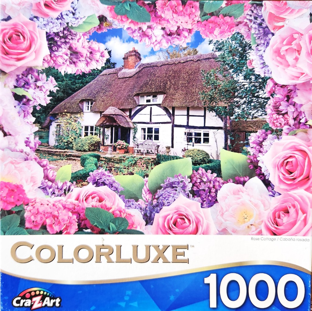 A traditional English cottage with a thatched roof viewed through a floral border of pink roses and purple lilacs.