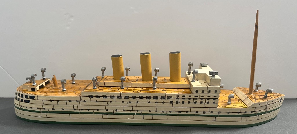 A three-dimensional wooden model of an ocean liner with three yellow smokestacks against a white background.