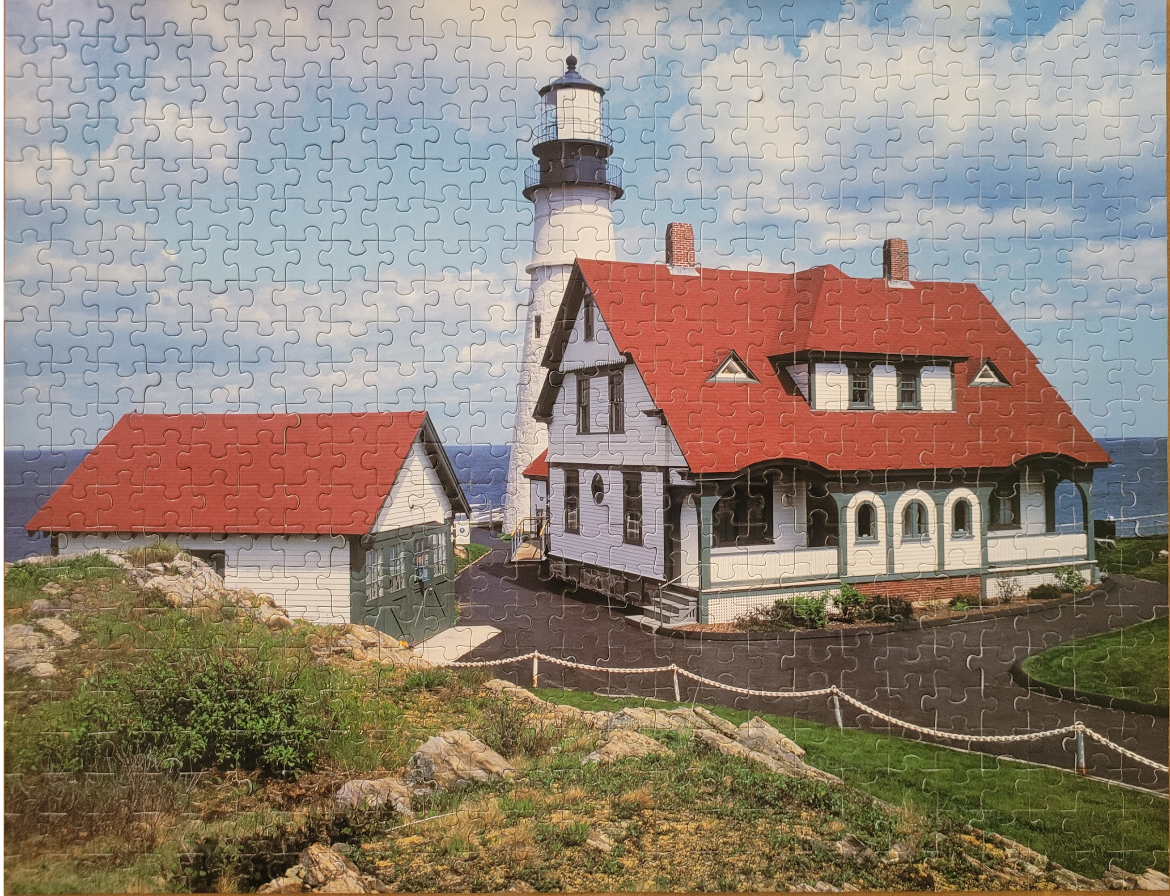 A lighthouse and keeper's cottage with red roofs overlooking a blue sea under a partly cloudy sky.