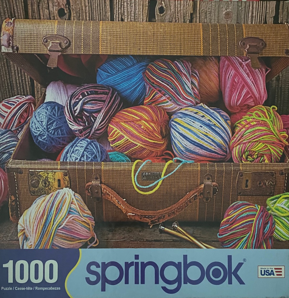 An open vintage suitcase filled with colorful yarn balls and knitting needles.