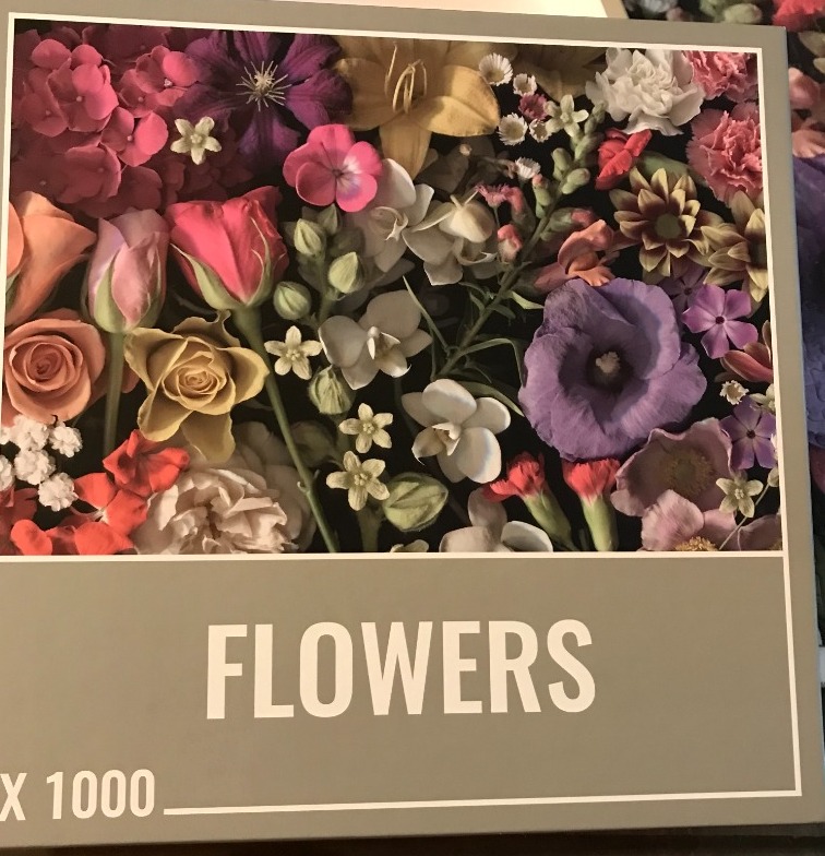A close-up photographic arrangement of various colorful flowers on a dark background.