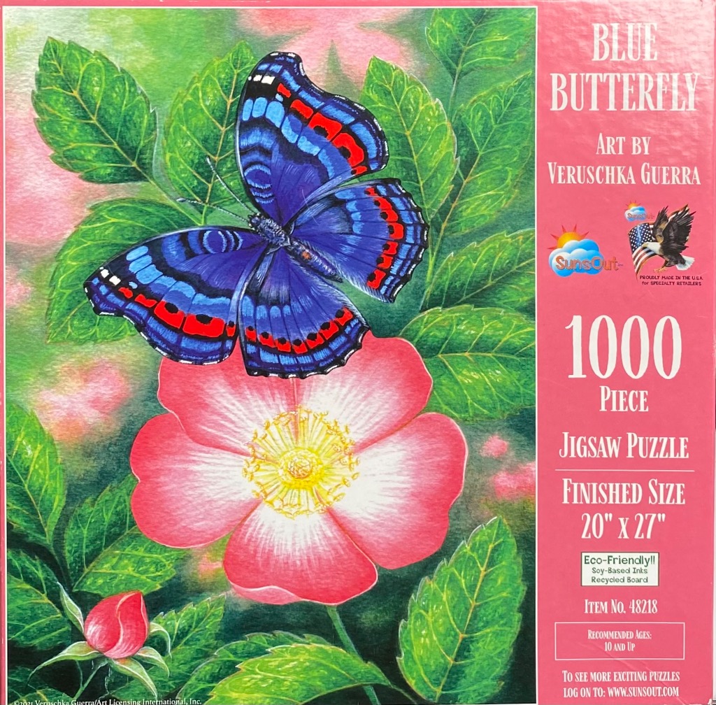 A vibrant blue butterfly with red accents perched on a large pink wild rose surrounded by lush green foliage.
