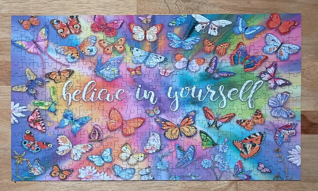A colorful collage of butterflies surrounding the text 'believe in yourself' on a rainbow watercolor background.