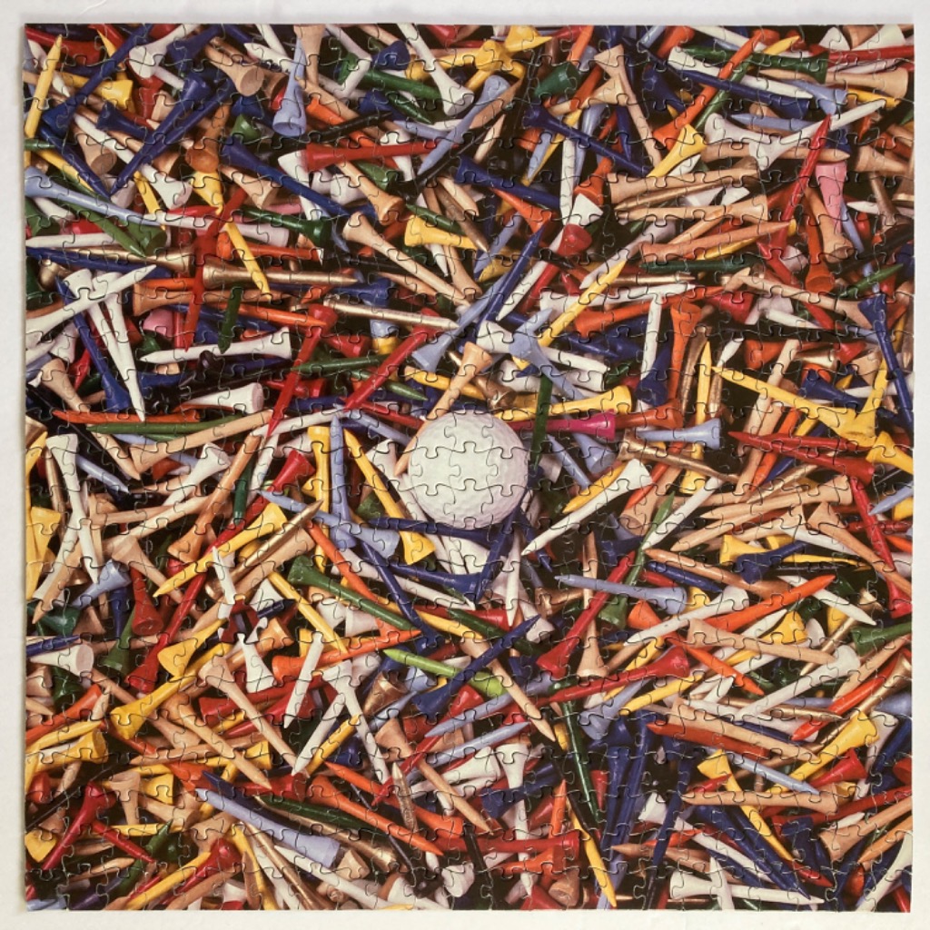 A central white golf ball surrounded by a dense, chaotic pile of colorful wooden golf tees.