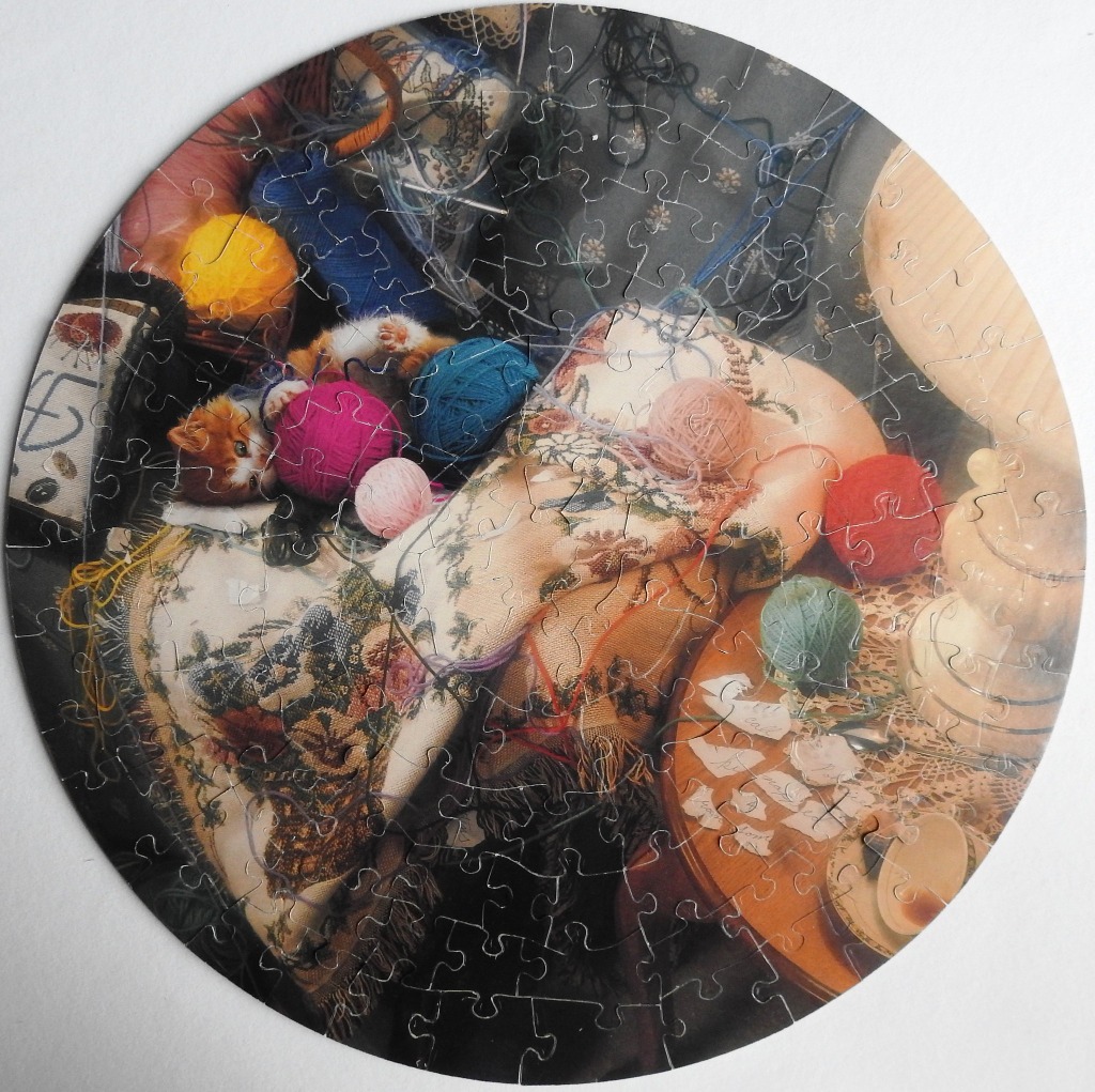 A playful ginger kitten nestled among various colorful yarn balls and embroidered fabrics.