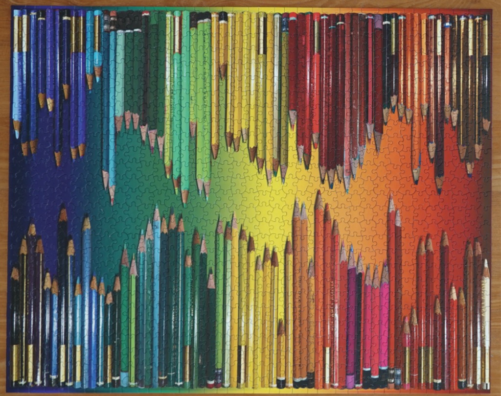 An array of sharpened coloured pencils arranged vertically in a vibrant spectrum against a gradient rainbow background.