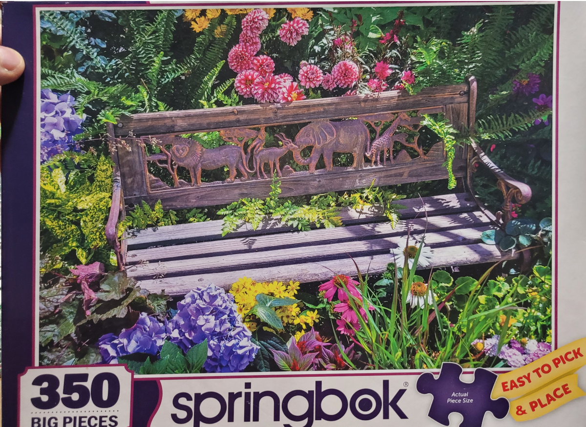 A wooden garden bench with carved animal figures set in a vibrant flower garden.
