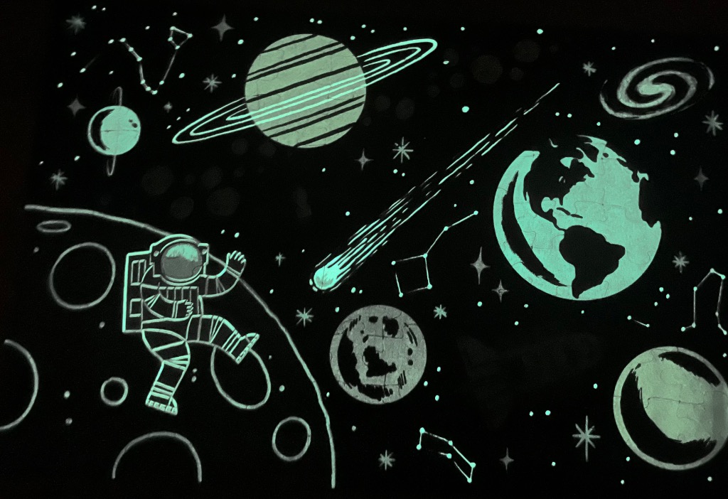 An illustration of an astronaut floating in space among planets, a comet, and constellations that glow in the dark.
