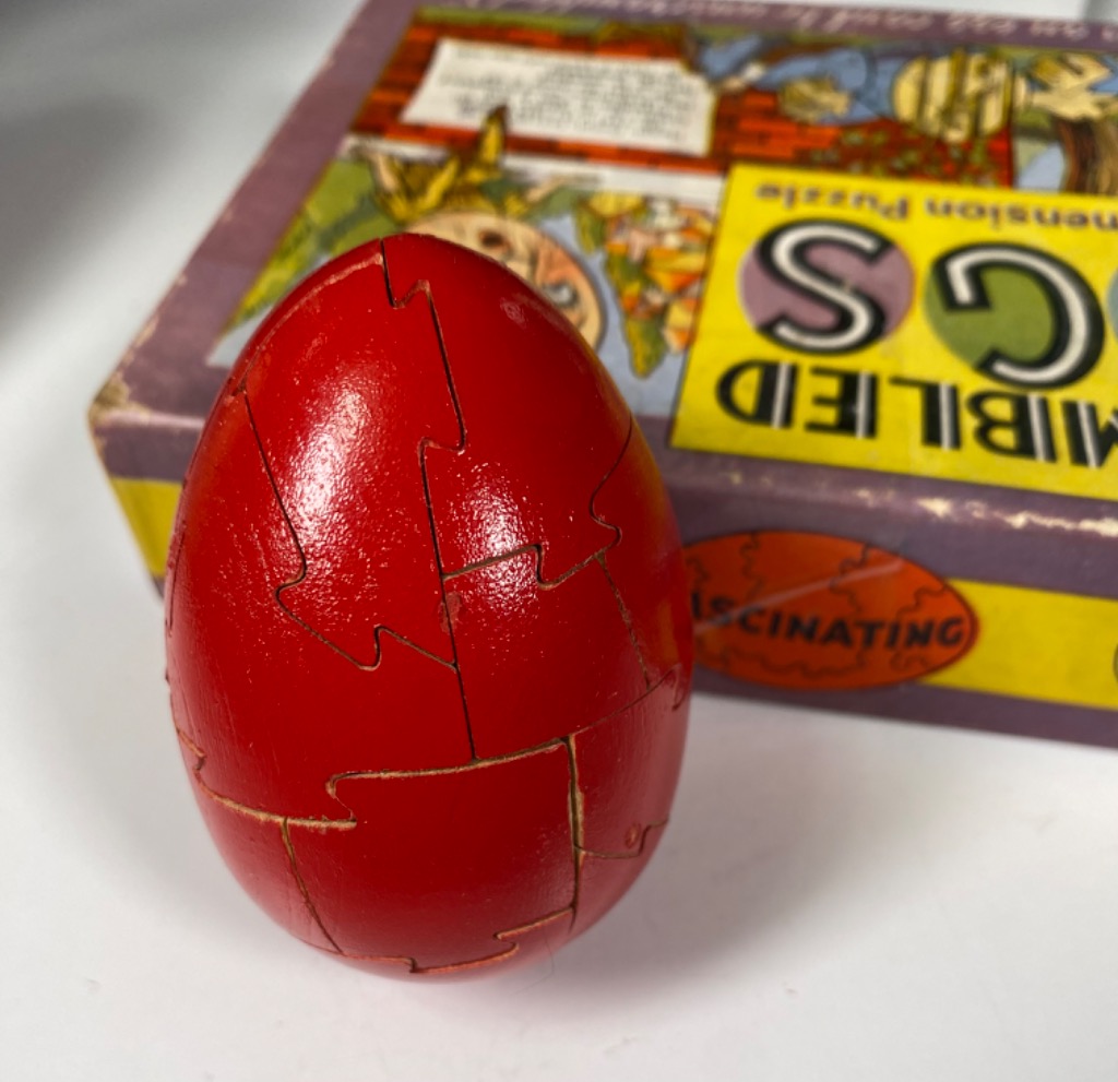 A bright red, egg-shaped object standing in front of a vintage illustrated box.