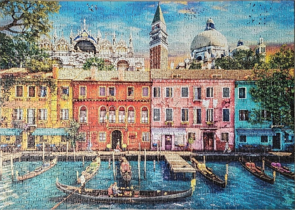 A colorful canal scene in Venice, Italy with gondolas, vibrant buildings, and distant domed architecture.