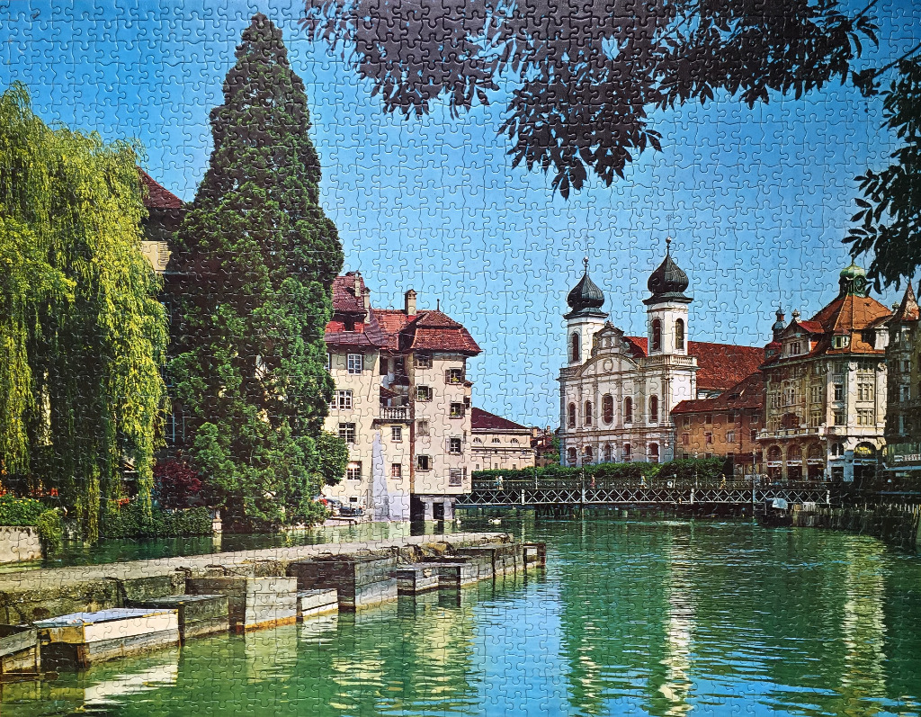 A riverside view of historic buildings and a twin-towered church in Lucerne, Switzerland.