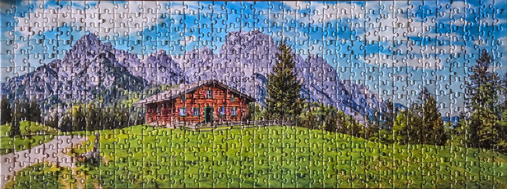 A traditional wooden alpine cabin nestled in a lush green meadow before jagged, snow-dusted mountains.