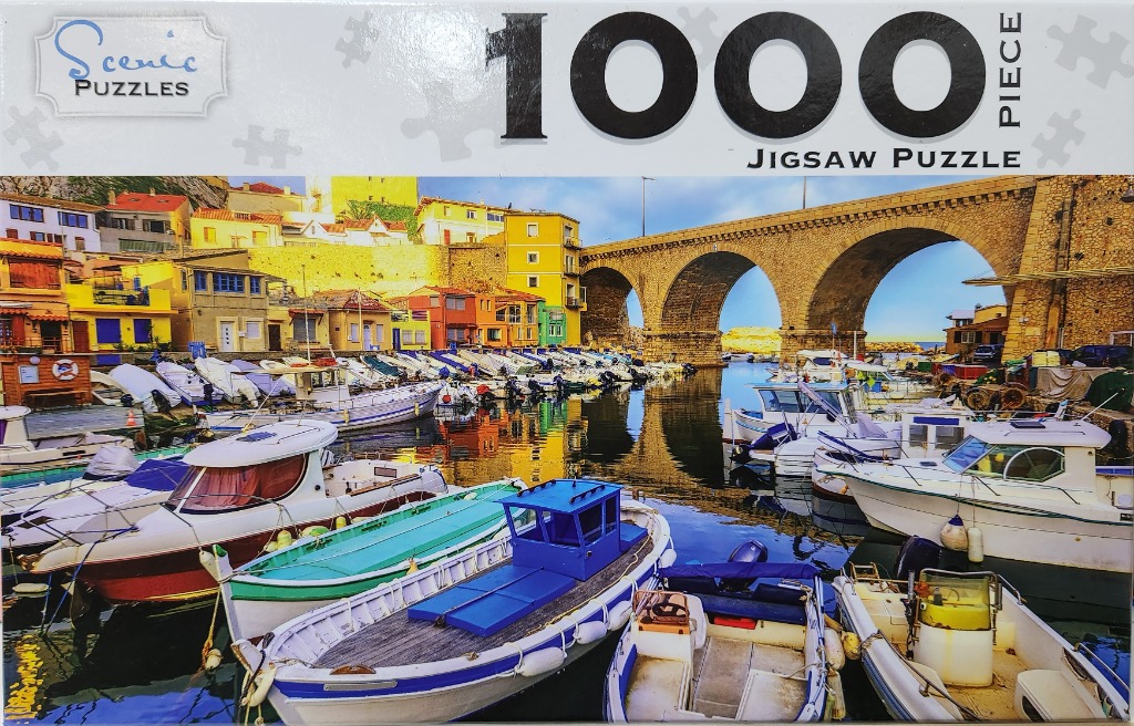 A sunny Mediterranean harbor with colorful boats and a stone arched bridge.