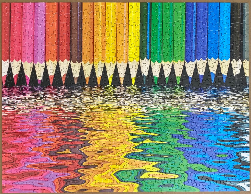 A row of colorful pencils reflecting in rippling water in a spectrum of colors.