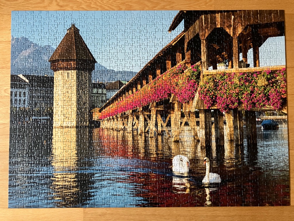 The Chapel Bridge in Lucerne, Switzerland with flowering baskets and swans on the water at sunset.