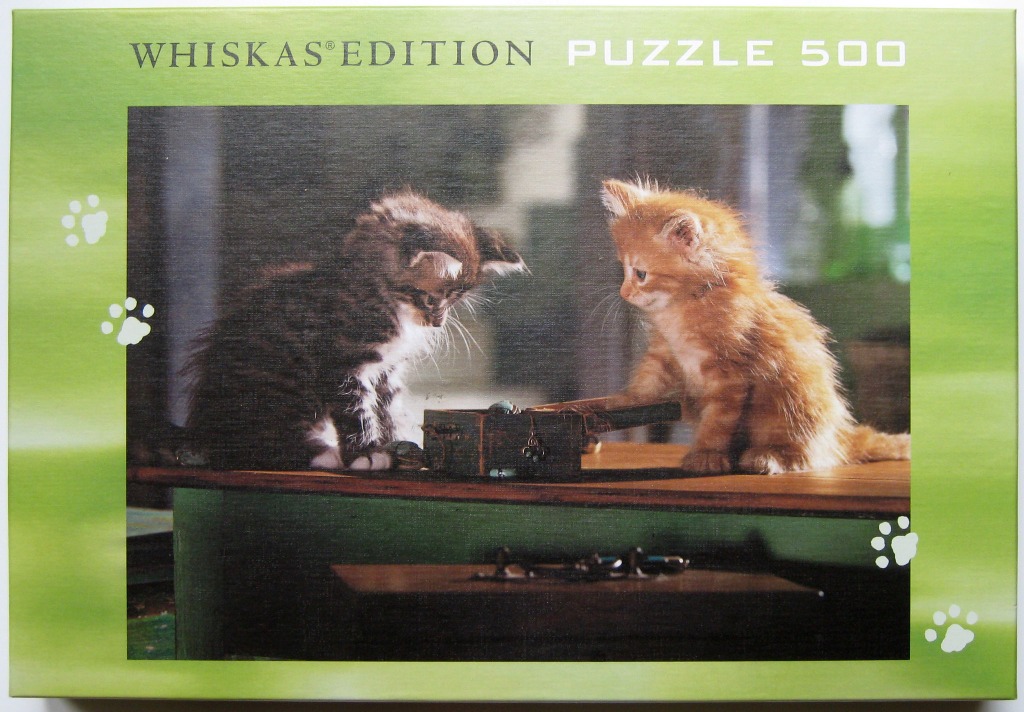 A fluffy tabby kitten and an orange kitten sitting on a table looking into a small wooden box.