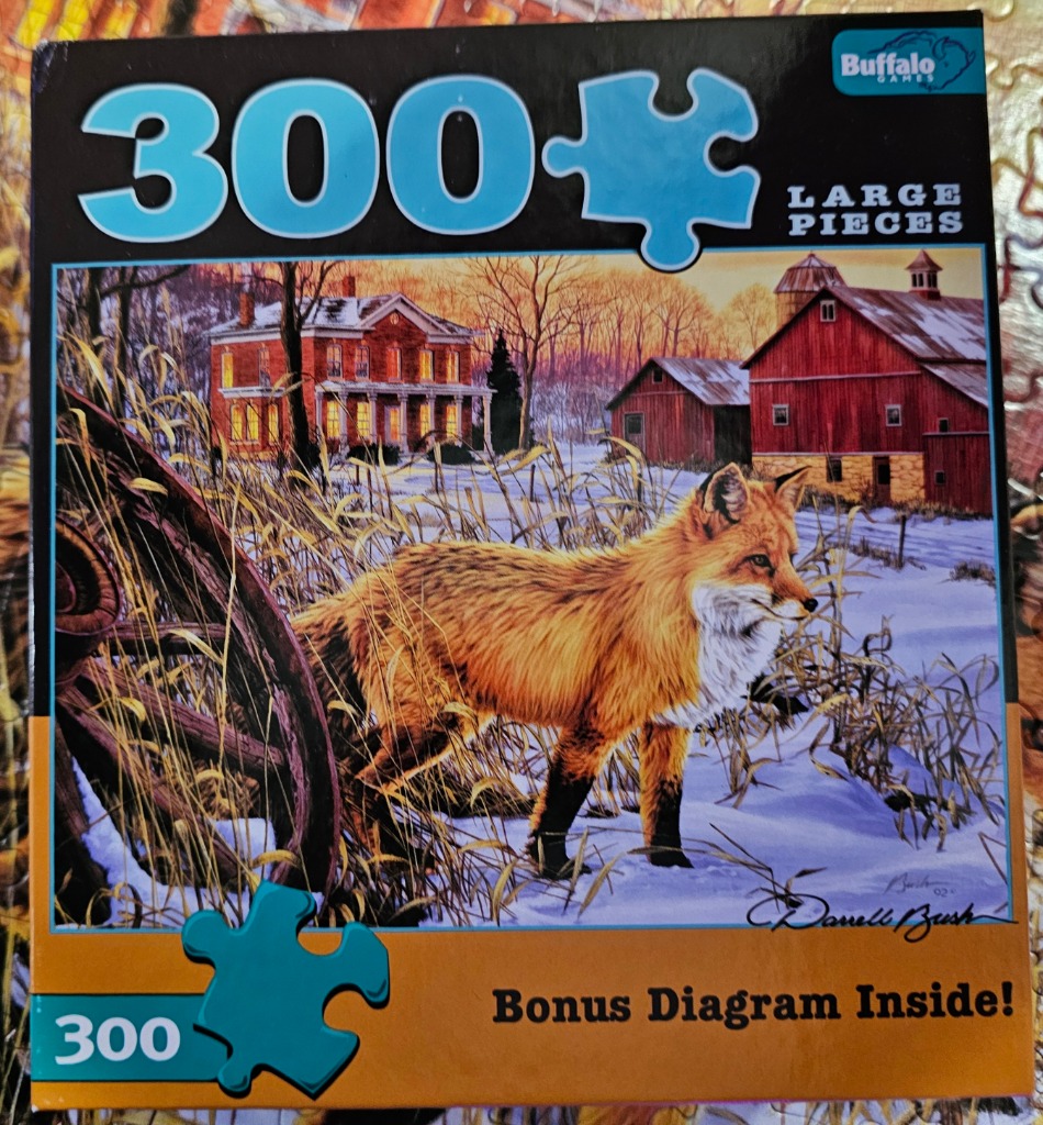 A red fox standing in a snowy field in front of a rustic red barn and farmhouse at sunset.