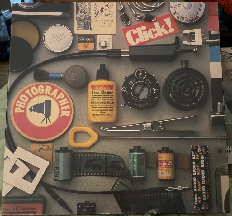 A flat-lay photograph of vintage photography equipment, film, and accessories arranged on a grey background.