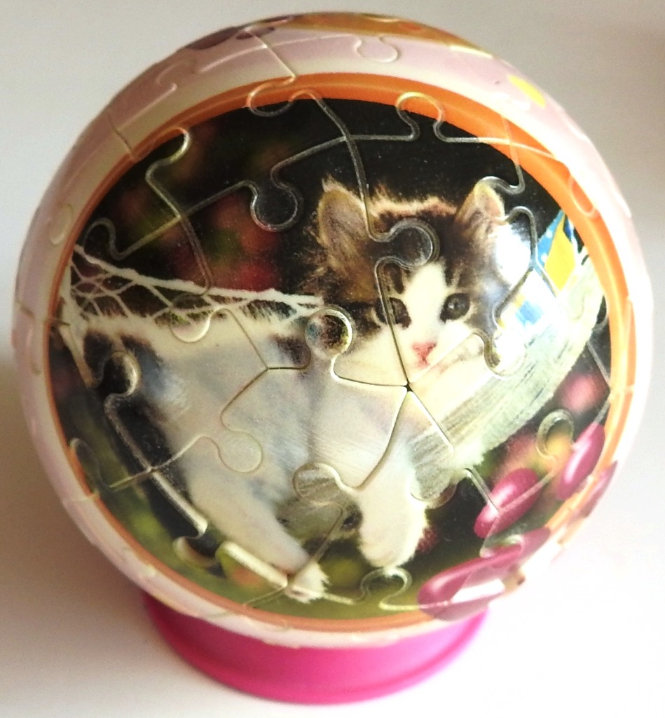 A spherical image featuring a fluffy kitten with brown and white fur on a decorated ball.