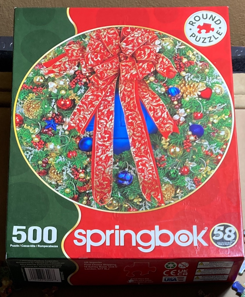 A circular photograph of a lush Christmas wreath decorated with a large red bow and festive ornaments.